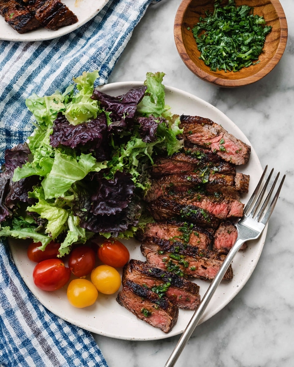 A white plate holds a simple meal with two main parts: on the left side, mixed dark purple and light green lettuce leaves form a fresh bed, topped with a few round red and one yellow cherry tomatoes, adding bright spots of color; on the right side, there are six pieces of sliced grilled steak, showing a pink center with charred edges and small green herb bits sprinkled on top. A silver fork rests on the right edge of the plate, partly under the steak. Nearby, a small wooden bowl filled with chopped green herbs sits on a white marbled surface next to a folded blue and white checkered cloth. Photo taken with an iphone --ar 4:5 --v 7