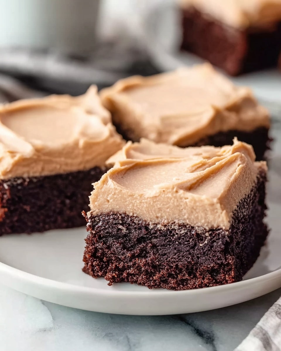 Three square pieces of chocolate cake are shown on a white plate placed on a white marbled surface. Each piece has a thick bottom layer of dark brown, soft, and moist chocolate cake with a dense texture. On top, there is a smooth, thick layer of light brown frosting that looks creamy and evenly spread, with slight swirls visible from spreading. The background is softly blurred, focusing on the rich color contrast between the dark cake and the light frosting. Photo taken with an iphone --ar 4:5 --v 7