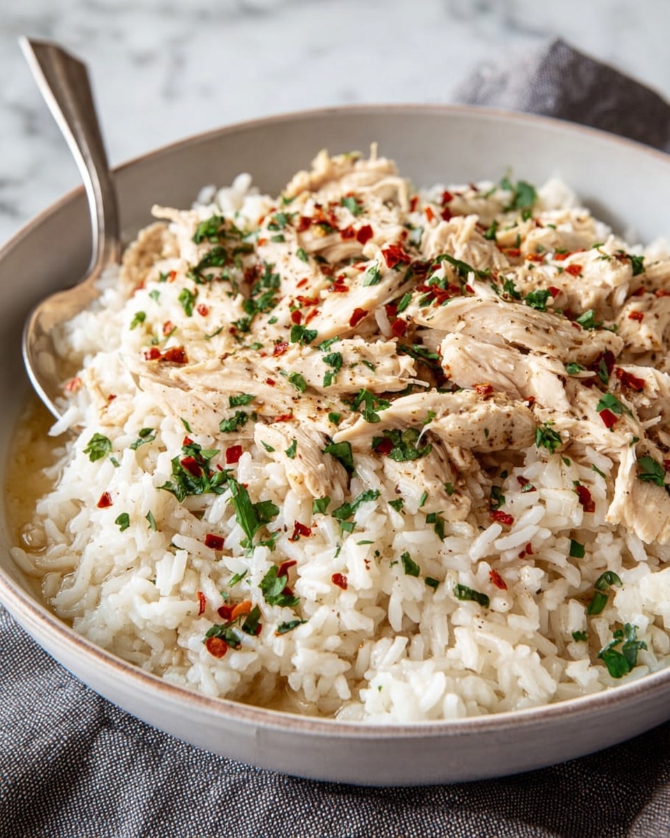 The dish shows creamy rice mixed with grilled chicken pieces on top, all covered in a white sauce that gives a glossy look. The chicken is golden brown with grill marks and is scattered evenly across the rice. Small green herb flakes are sprinkled over both the chicken and rice, adding color and freshness. The food is served in a deep white bowl with a shiny metal spoon placed inside it. The background is a white marbled texture. photo taken with an iphone --ar 4:5 --v 7