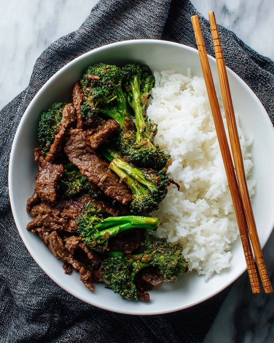 A white bowl holds two main parts: on one side, a generous portion of fluffy white rice with soft, distinct grains, and on the other side, a stir-fry of dark brown, glossy beef strips mixed with bright green broccoli florets that have a slightly charred texture. Resting on the edge of the bowl are a pair of wooden chopsticks placed diagonally. The bowl sits on a white marbled surface with a textured dark gray cloth underneath part of it. photo taken with an iphone --ar 4:5 --v 7