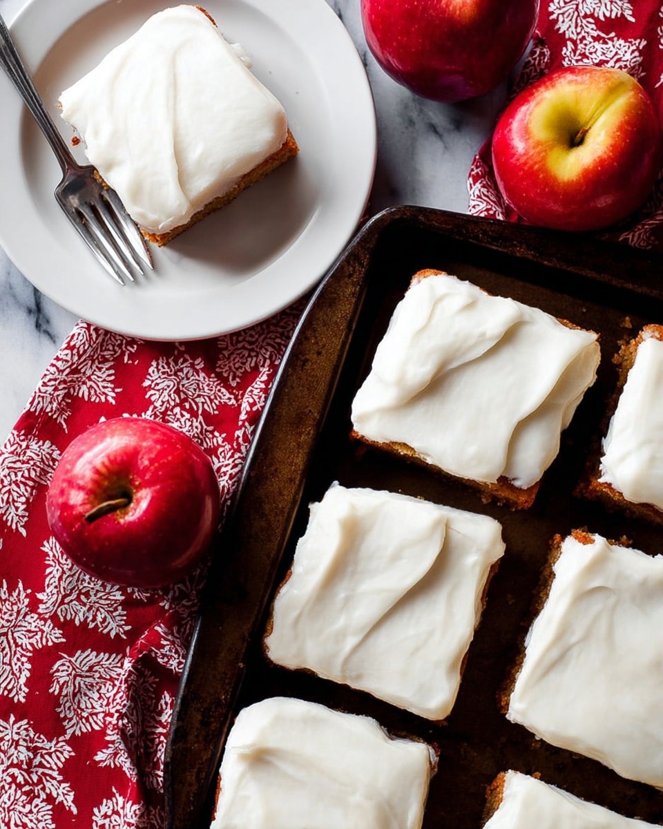 Six square pieces of cake with a thick, smooth layer of white frosting spread evenly on top are arranged on a dark baking tray. The cake itself is light brown and soft in texture. Two red apples with yellow highlights are placed near the top of the tray, adding a fresh contrast. To the left, one piece of cake is served on a white plate, accompanied by a silver fork resting on a red cloth with white patterns. The background is a white marbled texture. Photo taken with an iphone --ar 4:5 --v 7