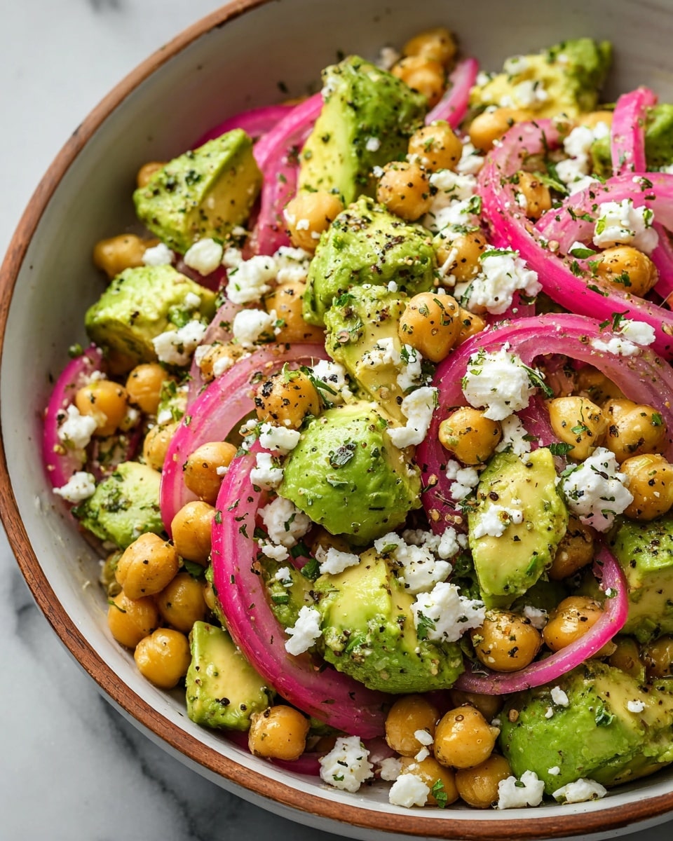 A close-up of a salad in a white bowl with a wooden rim, placed on a white marbled surface. The salad has several layers starting with whole chickpeas scattered throughout, giving a round and yellowish texture. Large chunks of green avocado with creamy texture are mixed in evenly. Thin slices of pinkish-red pickled onions add color contrast throughout. Crumbled white cheese is sprinkled on top, adding a soft and crumbly texture. Everything is seasoned with black pepper and finely chopped green herbs, giving a fresh and seasoned look. photo taken with an iphone --ar 4:5 --v 7