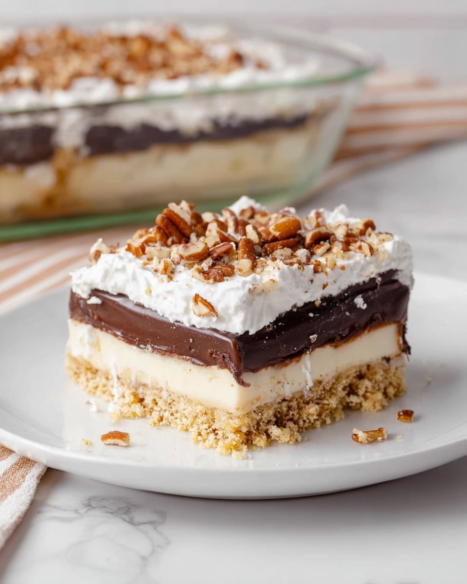 A square layered dessert sits on a white plate against a white marbled background. The bottom layer is a crumbly, light brown crust with a slightly rough texture. Above that is a smooth, pale cream layer, topped with a thick, glossy dark chocolate layer. On top of the chocolate is a fluffy white layer of whipped cream, sprinkled with chopped pecans that add a crunchy texture and warm brown color to the finish. In the background, a clear glass dish holds the rest of the dessert. photo taken with an iphone --ar 4:5 --v 7