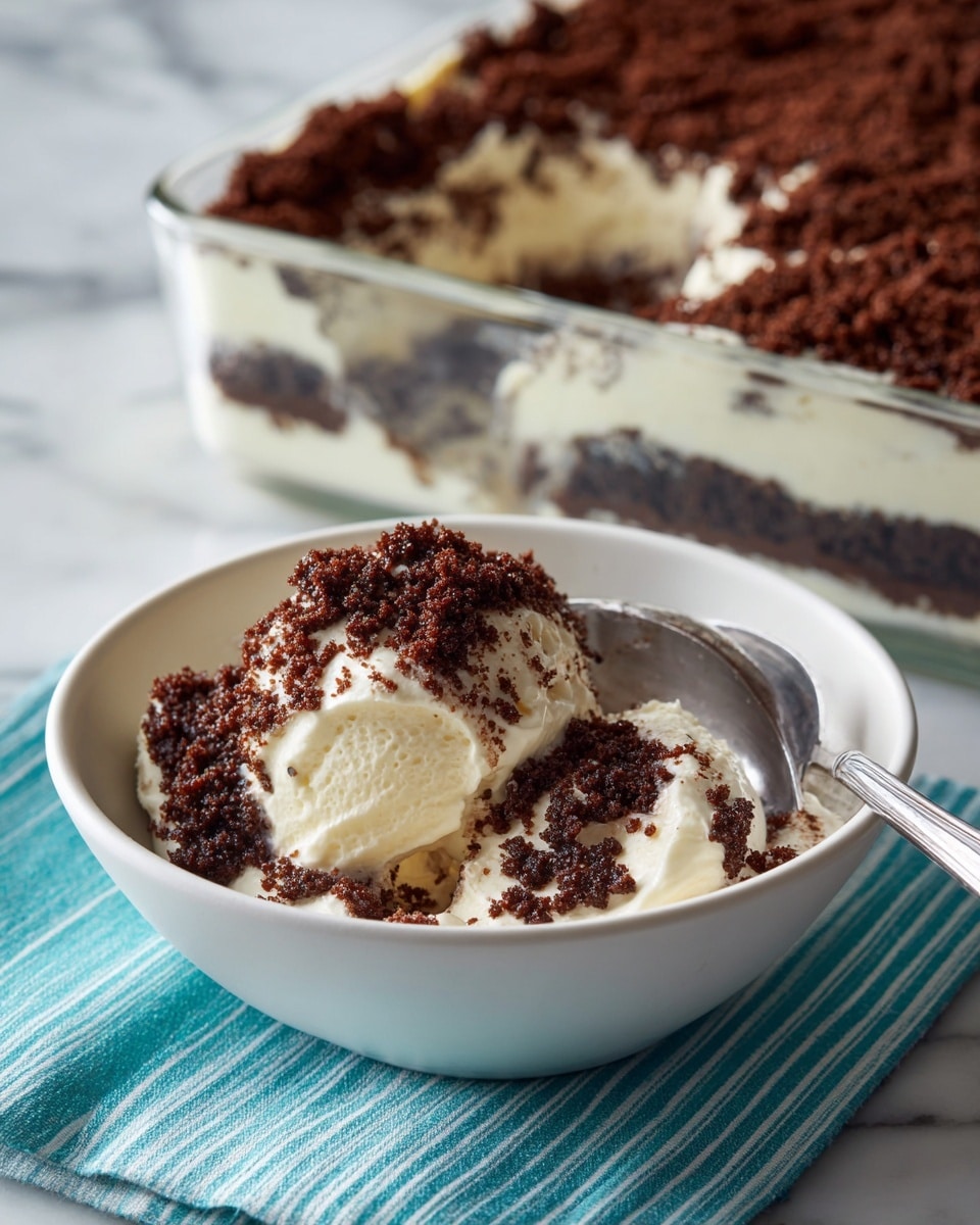 A close-up of a white bowl holding a creamy dessert with three scoops of smooth, white cream covered with a thick layer of fine, dark brown crumb topping, giving it a textured and slightly crumbly look. A silver spoon rests inside the bowl on the right side, partially scooping into the dessert, showing the creamy inside beneath the crumbs. Behind the bowl is a rectangular glass dish with three visible layers: a bottom layer of dark crumb, a thick middle layer of smooth, white cream, and a thick top layer of dark crumb topping. The entire scene is set on a white marbled surface with a turquoise and white striped cloth partially visible under the bowl. Photo taken with an iphone --ar 4:5 --v 7