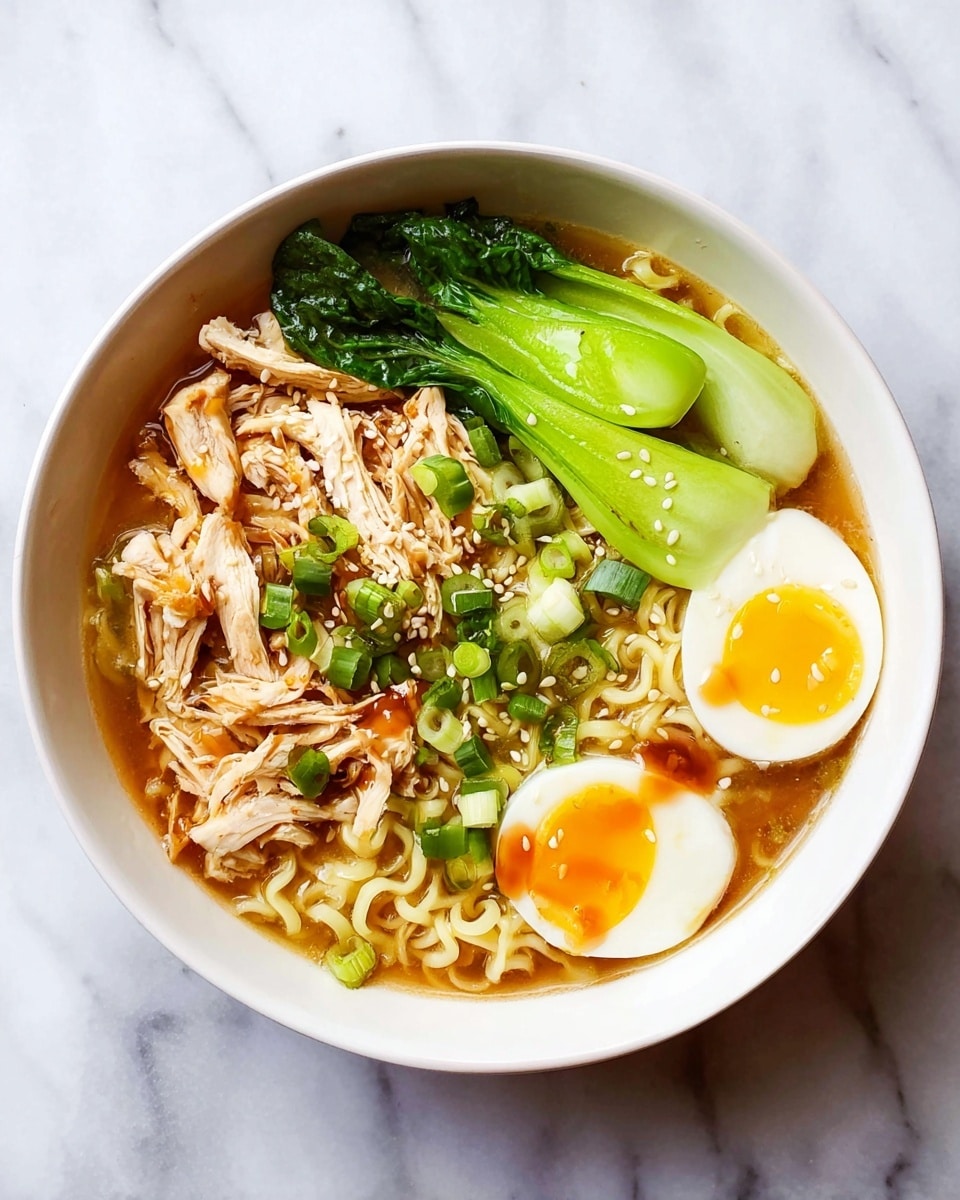 A white bowl filled with light brown broth as the base layer, topped with a nest of curly, pale yellow ramen noodles slightly off-center. On the left side are pieces of shredded light brown chicken breast with a few drizzles of sauce. To the right, there are three bright green bok choy leaves. A halved soft-boiled egg with a smooth white edge and a bright yellow yolk sits near the bottom right. Scattered green onion slices and white sesame seeds are sprinkled over the noodles and chicken. The bowl rests on a white marbled surface. Photo taken with an iphone --ar 4:5 --v 7