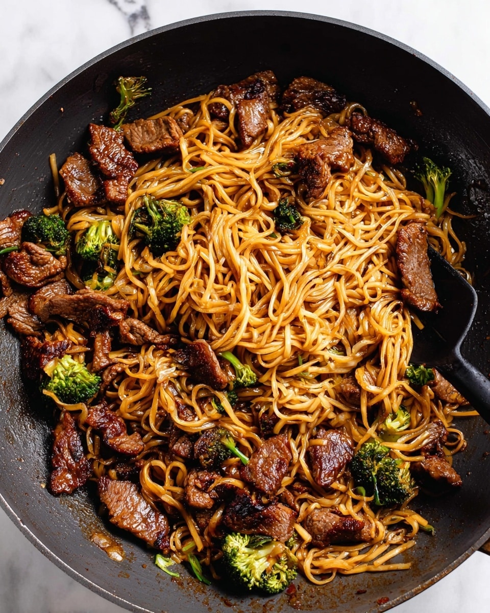 A white plate filled with a bed of cooked spaghetti noodles colored light brown from sauce, mixed with dark brown cooked beef pieces that have a shiny glaze, and bright green broccoli florets scattered throughout. The top of the dish is sprinkled with small white sesame seeds, adding texture and contrast. A fork rests on the right side of the plate, slightly tangled in the noodles. The plate sits on a white marbled surface, with a second plate partially visible in the top left corner and a floral patterned cloth with orange and brown flowers in the upper right area. Photo taken with an iphone --ar 4:5 --v 7