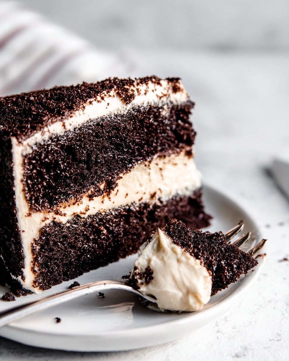 A close-up view of a two-layer dark chocolate cake with thick light cream filling between the layers and on the sides, resting on a white plate on a white marbled surface. The dark cake layers have a moist, crumbly texture, and the cream layers are smooth and light. A piece of the cake is cut and placed on a silver fork that lies on the plate, showing the cream and cake mix together. Photo taken with an iphone --ar 4:5 --v 7