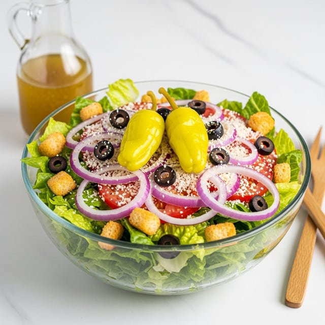 A clear glass bowl on a white marbled surface holds a fresh salad with several layers and colors: the base layer is light green crisp lettuce, topped with thin slices of purple onion and red tomato, scattered with small black olives and golden brown croutons, and finished with two bright yellow pepperoncini peppers standing out. The salad is lightly sprinkled with shredded white cheese, adding a soft texture on top. A glass bottle with dressing sits nearby, along with wooden utensils partially visible at the side. Photo taken with an iphone --ar 4:5 --v 7