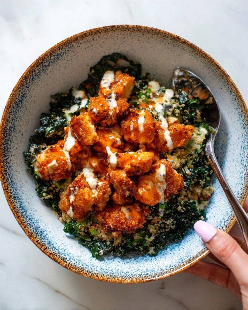 A white bowl with a speckled blue and brown interior holds a layered dish starting with dark green kale at the bottom, which looks slightly wilted and mixed with a light, crumbly topping. On top, there are many pieces of golden-brown crispy chicken covered in a glossy orange sauce and drizzled with a creamy white dressing. A spoon rests in the bowl on the right side, and a woman's hand with light pink nail polish holding the bowl's edge is visible at the bottom right. The bowl sits on a white marbled surface. photo taken with an iphone --ar 4:5 --v 7