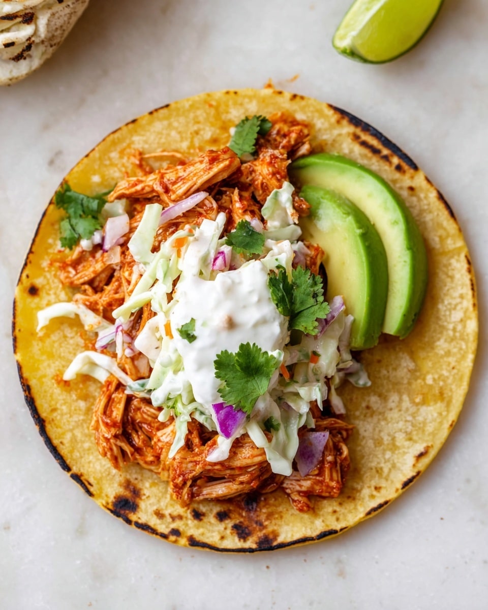 A single toasted yellow corn tortilla with charred edges sits flat on a white marbled surface, forming the base layer. On top, there is a thick layer of shredded reddish-orange chicken, followed by a scoop of creamy coleslaw made from thin strips of white and purple cabbage mixed with small bits of carrot and fresh green cilantro. Thin slices of fresh green avocado are arranged on one side, and a spoonful of white sour cream with a small cilantro leaf rests on the coleslaw. A bright green lime wedge is placed on the right edge of the tortilla. Photo taken with an iphone --ar 4:5 --v 7