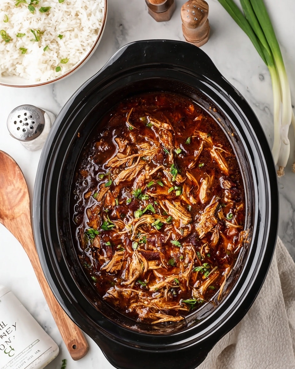 The image shows a black slow cooker filled with shredded chicken cooked in a thick, dark brown sauce, with some small bright green chopped herbs sprinkled on top. The chicken pieces are tender and soaked in the glossy sauce, giving an overall rich and savory look. Surrounding the slow cooker are a white bowl with cooked white rice, a wooden spoon resting on a white marbled surface, a pair of salt and pepper shakers, some green onion stalks, and a white container labeled “Oh honey honey.” The setting is bright, and the textures of the food and utensils are clearly visible. Photo taken with an iphone --ar 4:5 --v 7