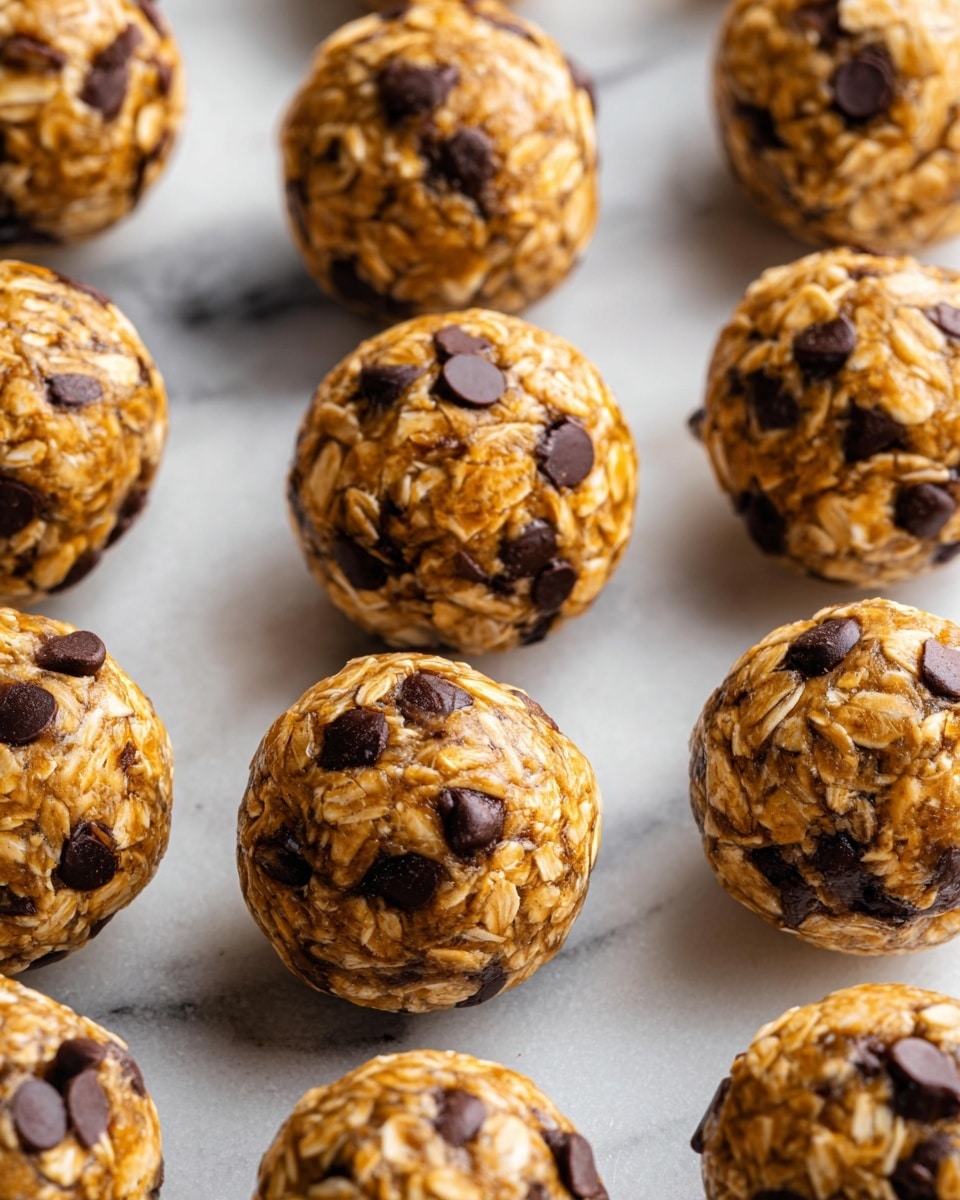 The image shows several round energy balls placed close to each other on a white marbled surface. Each ball has a rough texture made of light brown oats mixed with dark brown chocolate chips that are embedded on the surface evenly. The energy balls have a soft and chewy look with visible oat flakes and glossy chocolate spots scattered across the golden brown base. The lighting highlights the texture and colors clearly. photo taken with an iphone --ar 4:5 --v 7