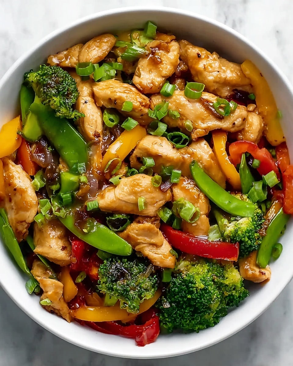 A close-up view of a white bowl filled with a colorful stir-fry dish showing multiple layers. The bottom layer has mixed cooked vegetables including vibrant green broccoli florets, bright red and yellow bell pepper strips, and light green snap peas. Above the vegetables are golden-brown pieces of cooked chicken with a slightly glossy sauce coating them, adding a shiny texture. Small bits of chopped green onions are scattered on top, enhancing the fresh look. The bowl sits on a white marbled surface, making the colors of the dish pop. photo taken with an iphone --ar 4:5 --v 7