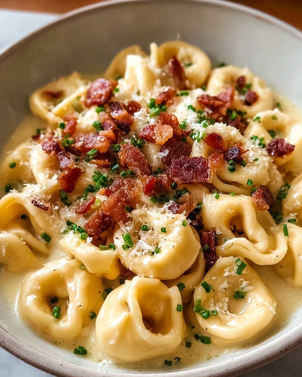 A close-up of a bowl with creamy tortellini pasta coated in a smooth light yellow cheese sauce, topped with small crispy brown bacon bits scattered evenly on top, and sprinkled with finely chopped green herbs and some grated white cheese. The pasta rings are plump and soft, filling the bowl fully, sitting on a white marbled texture. Photo taken with an iphone --ar 4:5 --v 7